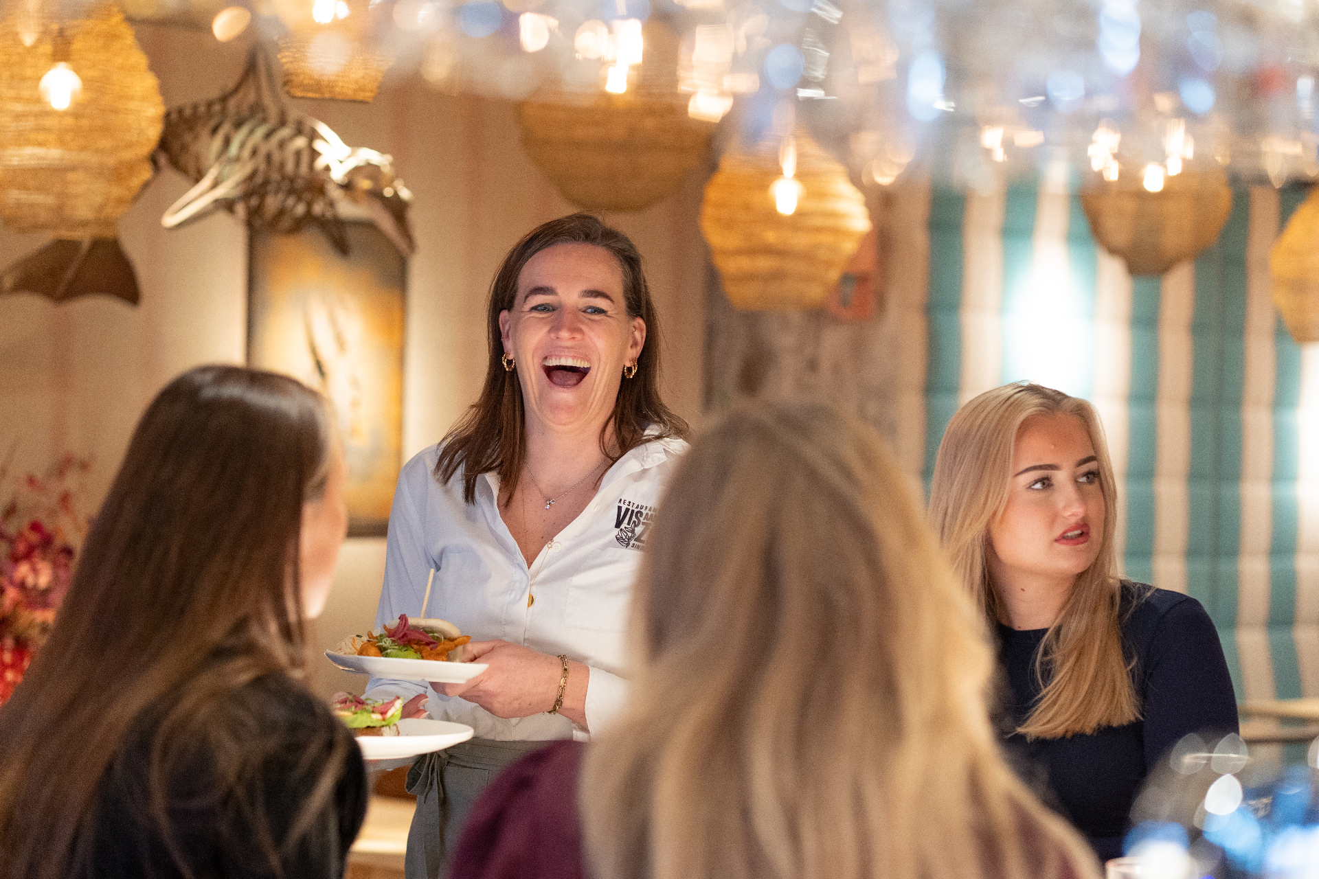 Marit Dekker serveert lachend gerechten aan gasten in Restaurant Vis aan Zee