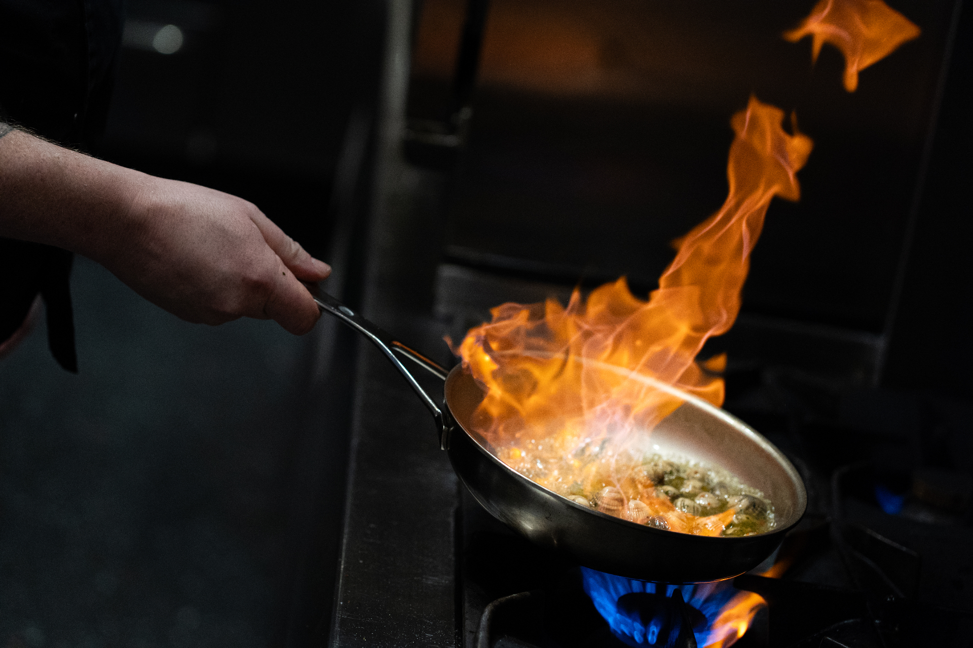 Kokkels worden geflambeerd in een koperen pan in de keuken van Vis aan Zee
